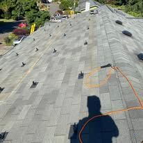 Gray shingled roof with a visible shadow and orange rope, viewed from above