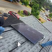 Solar panels being installed on a gray shingled roof, with workers visible and a suburban street below.