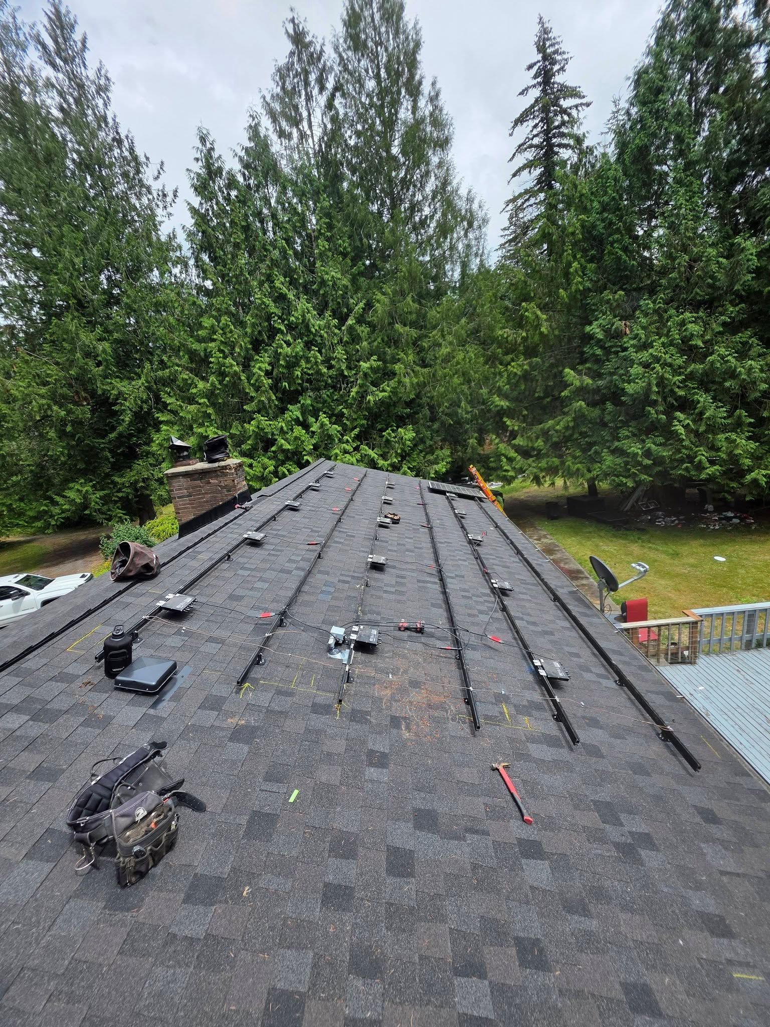 Roof under repair with scattered shingles, chimney, and tall trees in the background