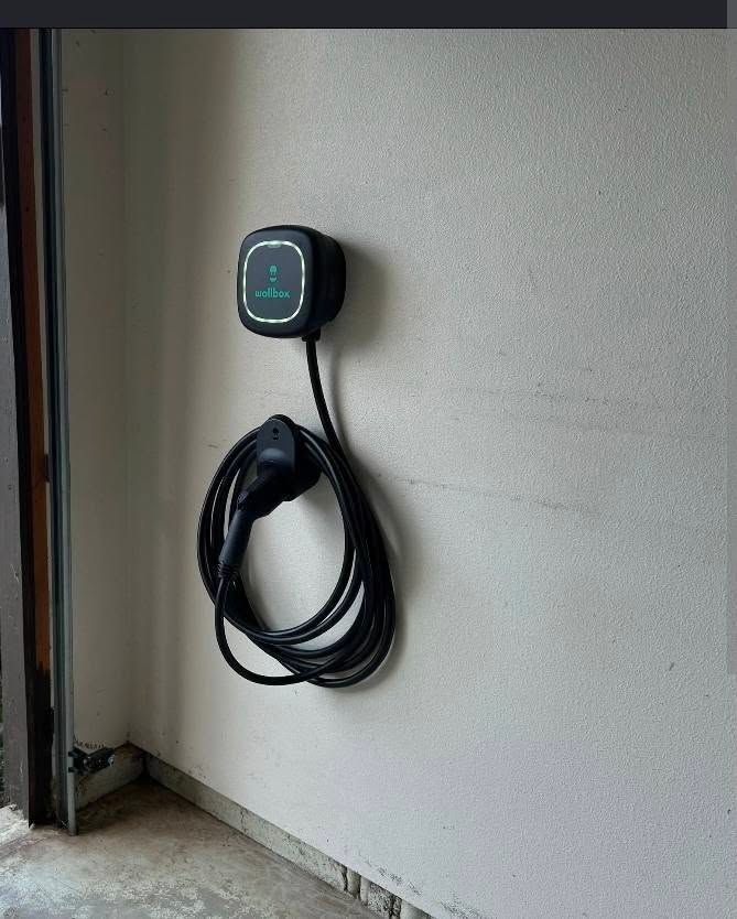 Wall-mounted EV charging unit with coiled black cable beside a garage wall
