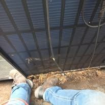 Two feet in jeans and sneakers standing on dirt beside a black metal fence