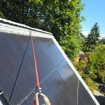 Person washing a slanted solar panel roof with a hose outdoors among trees