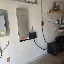 Wall-mounted electrical panels and conduit in a utility room with shelves and storage bins
