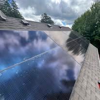 Solar panels on a sloped residential roof reflecting clouds and sky.