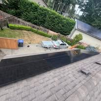 Backyard patio with a black retaining wall, outdoor lounge chairs, and potted plants beside a sloped hedge