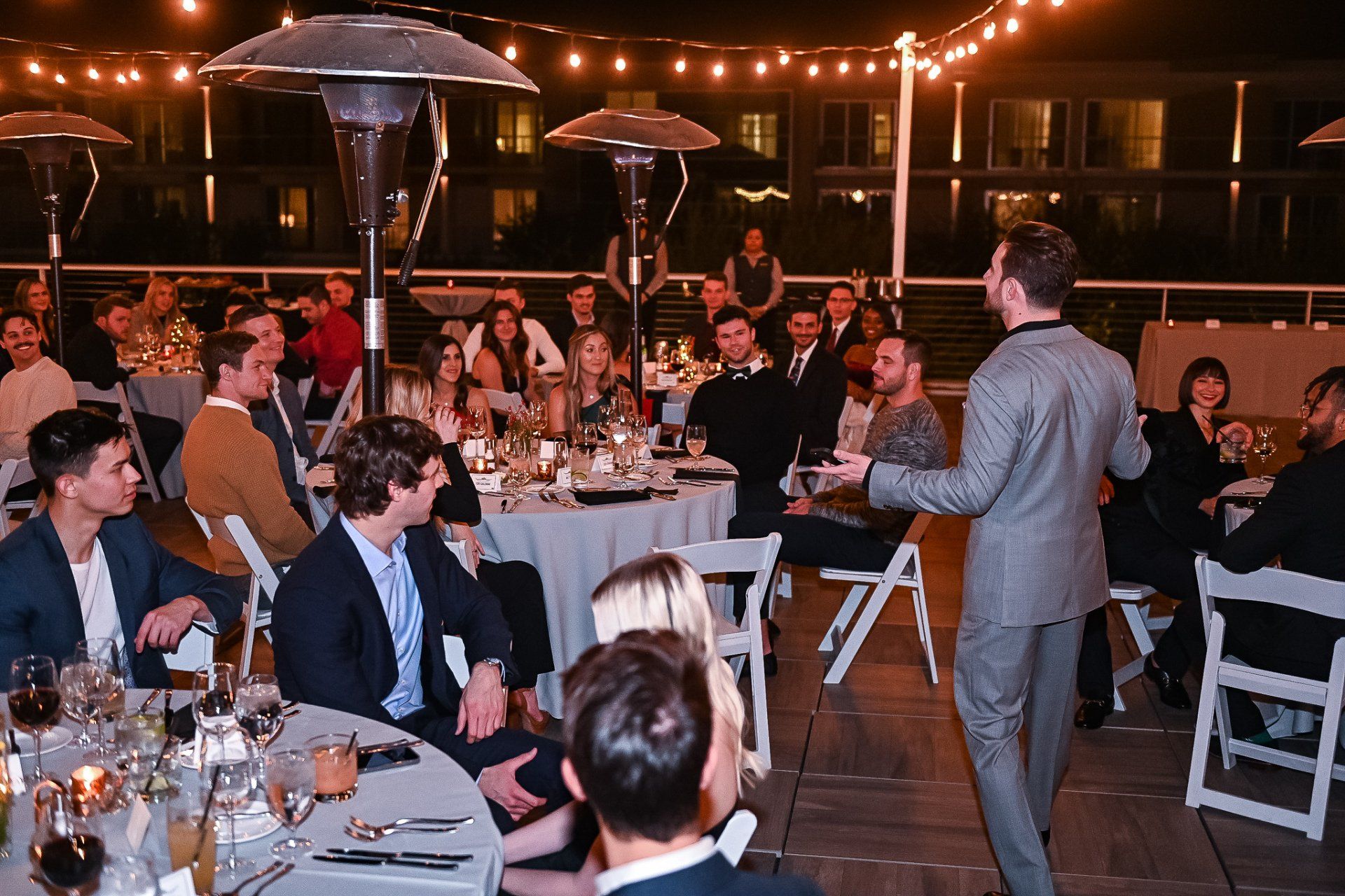 A man is standing in front of a crowd of people at a dinner party.