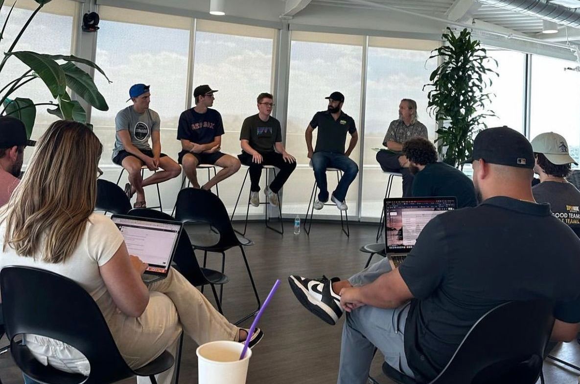 A group of people are sitting in a circle in a room with laptops.