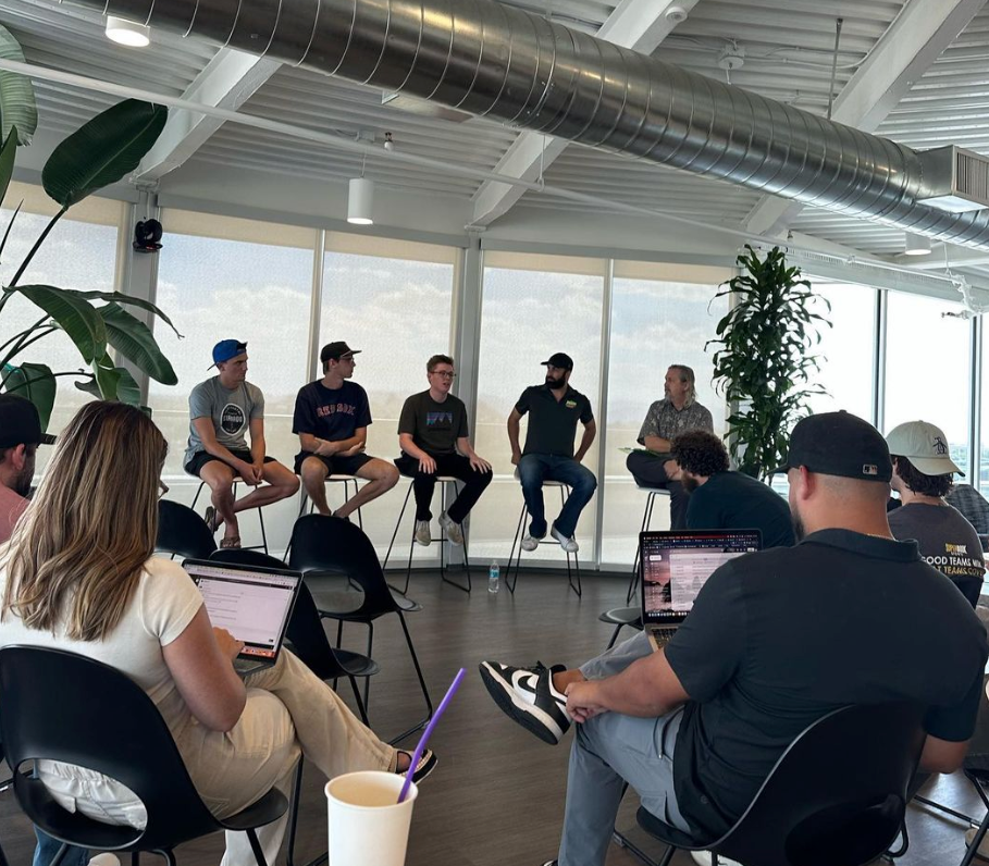 A group of people are sitting around a table with laptops