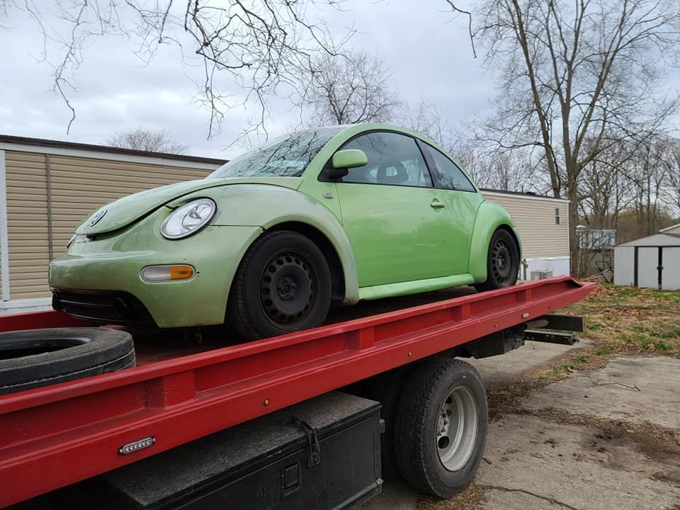 A green beetle is sitting on top of a red tow truck.
