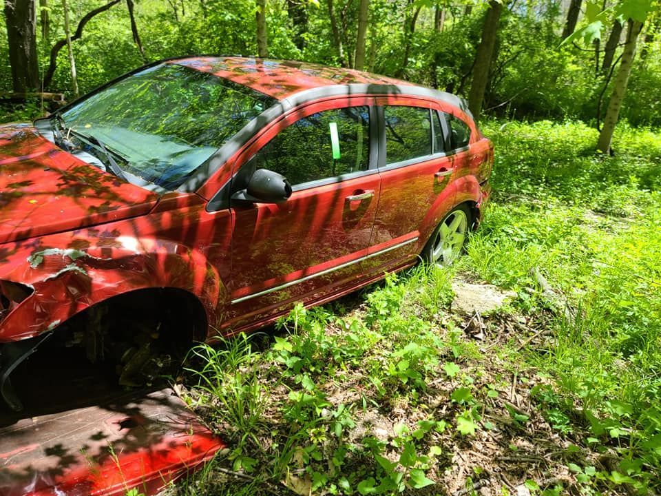 A red car is sitting in the middle of a forest.