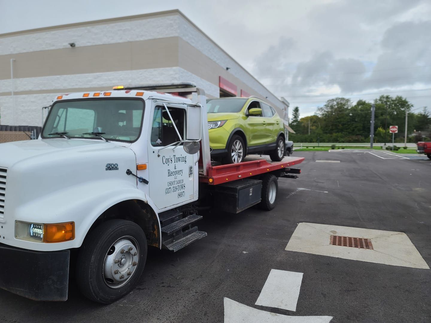 A tow truck with a green suv on the back is parked in a parking lot.