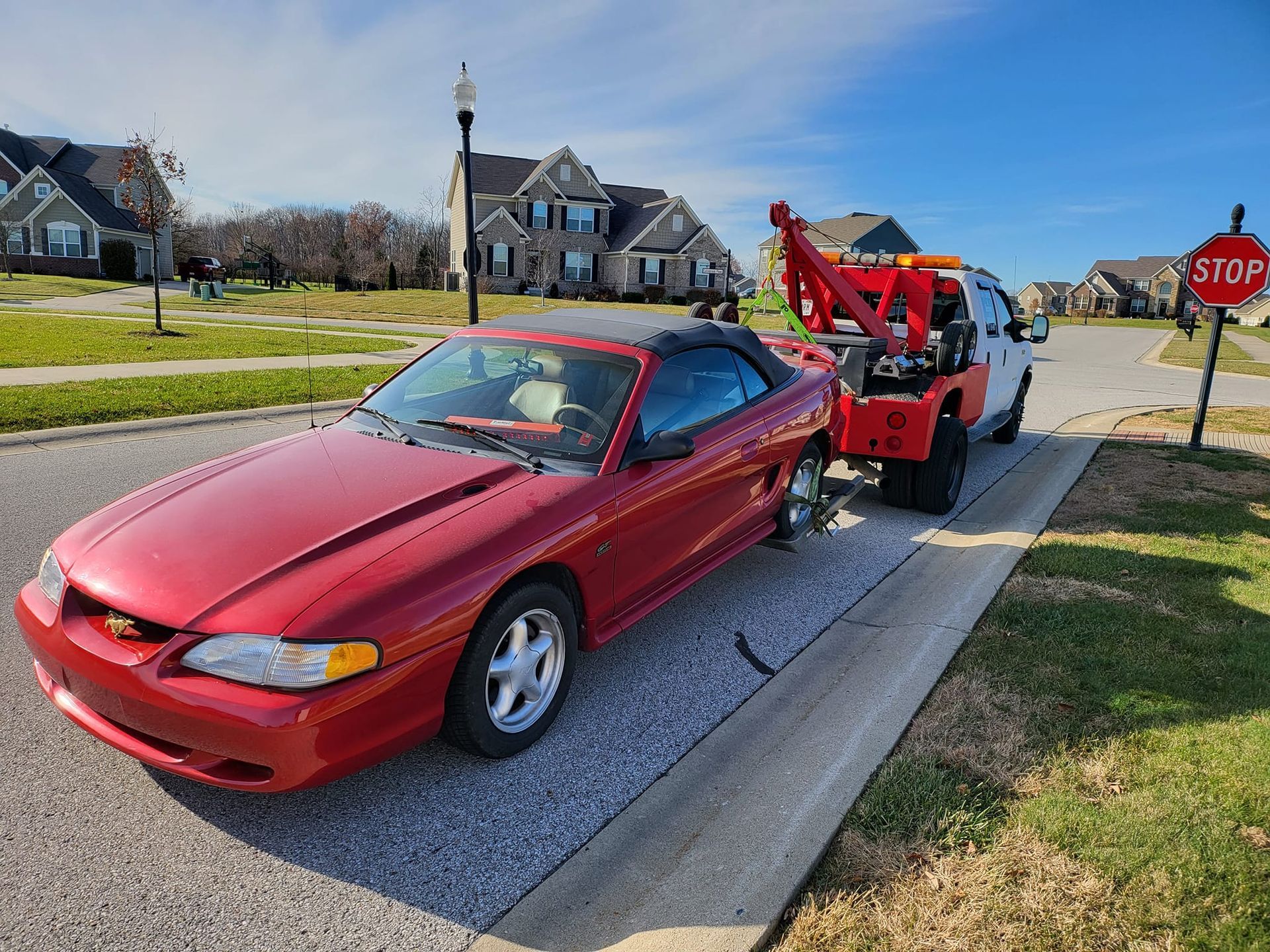 A red mustang is being towed by a tow truck.