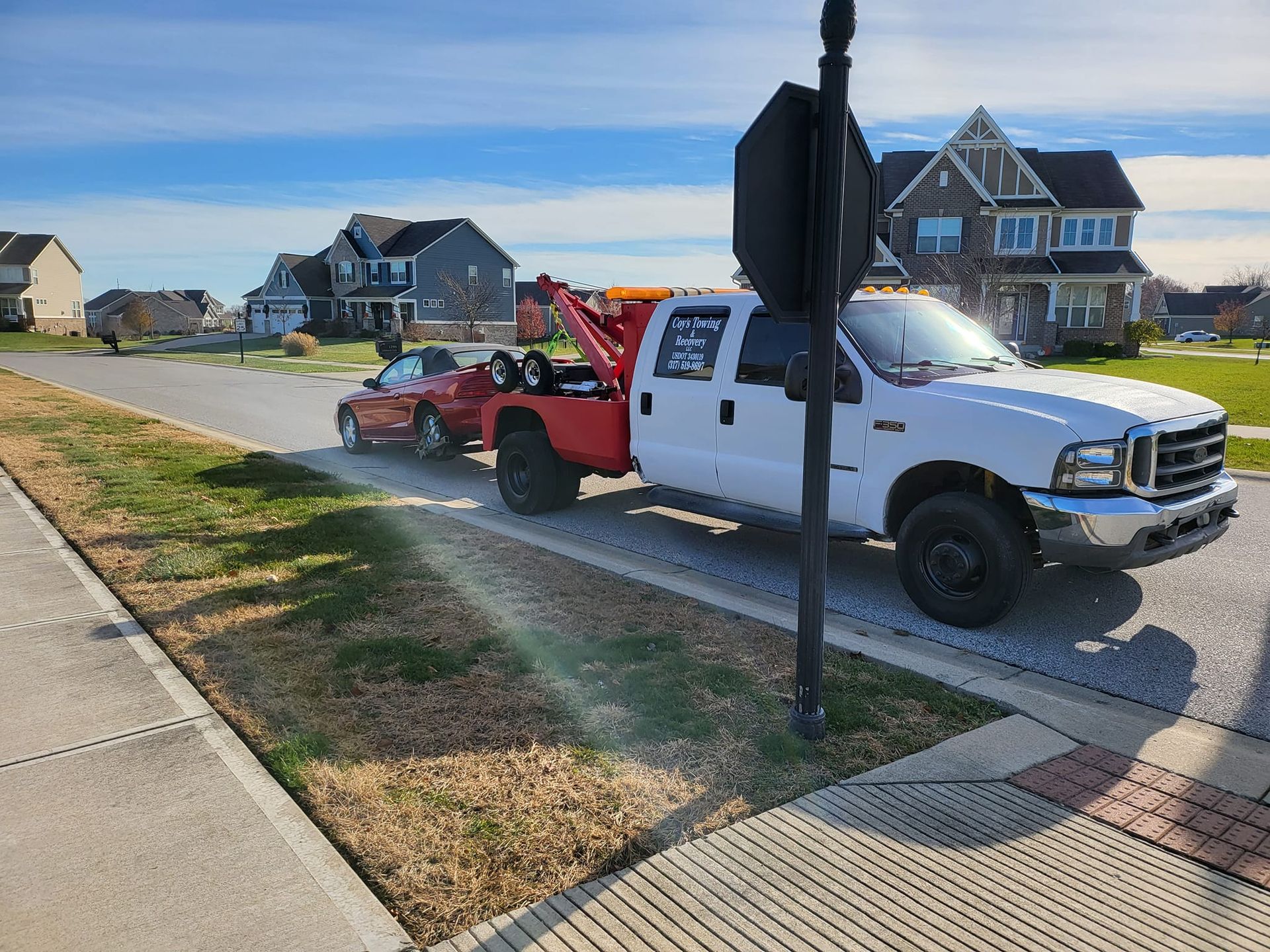 A white tow truck is towing a red car down a street.