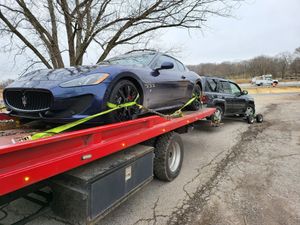 A blue maserati is sitting on top of a red tow truck.