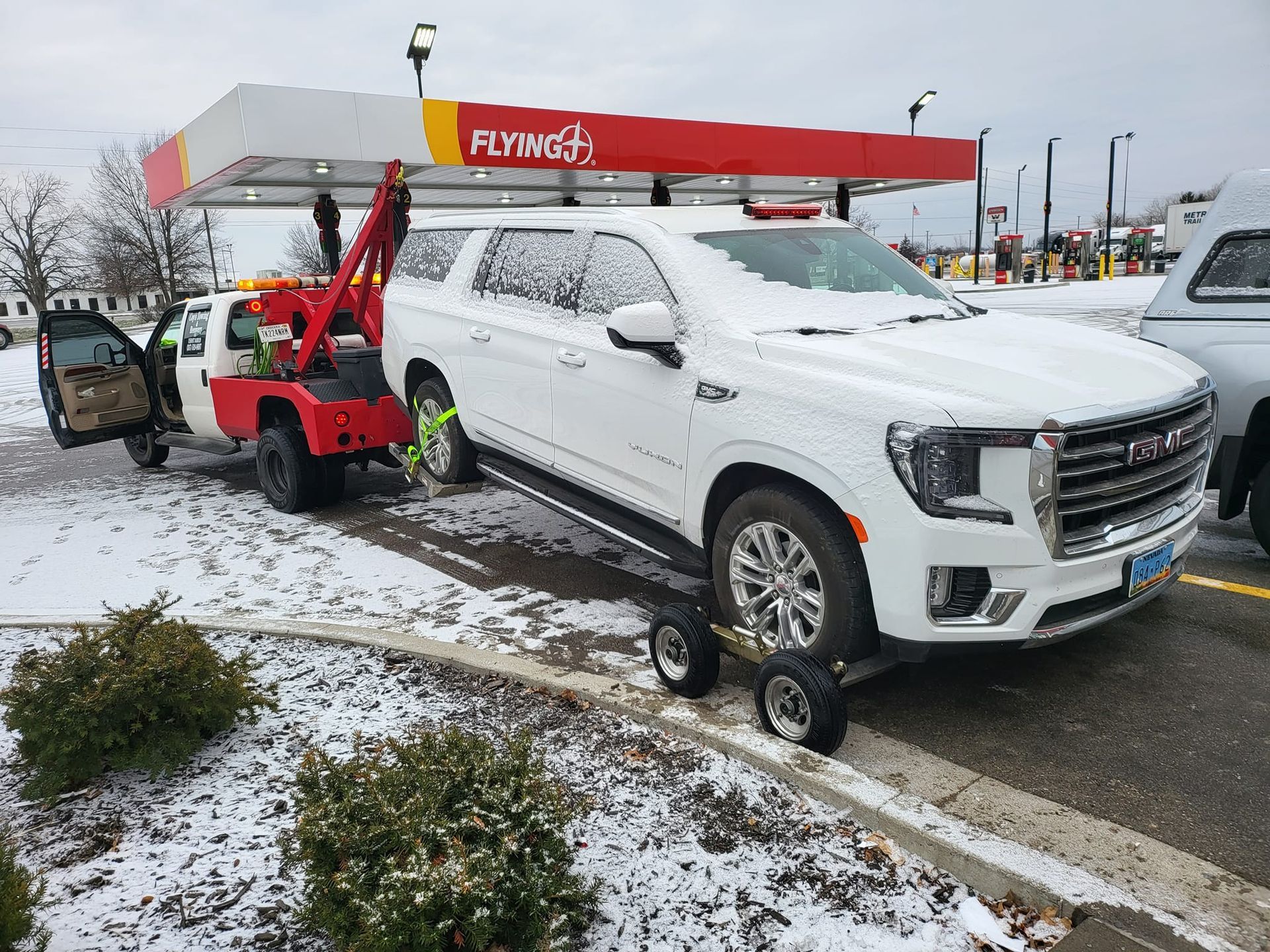 A white suv is being towed by a tow truck in a parking lot.