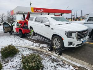 A white suv is being towed by a tow truck in a parking lot.