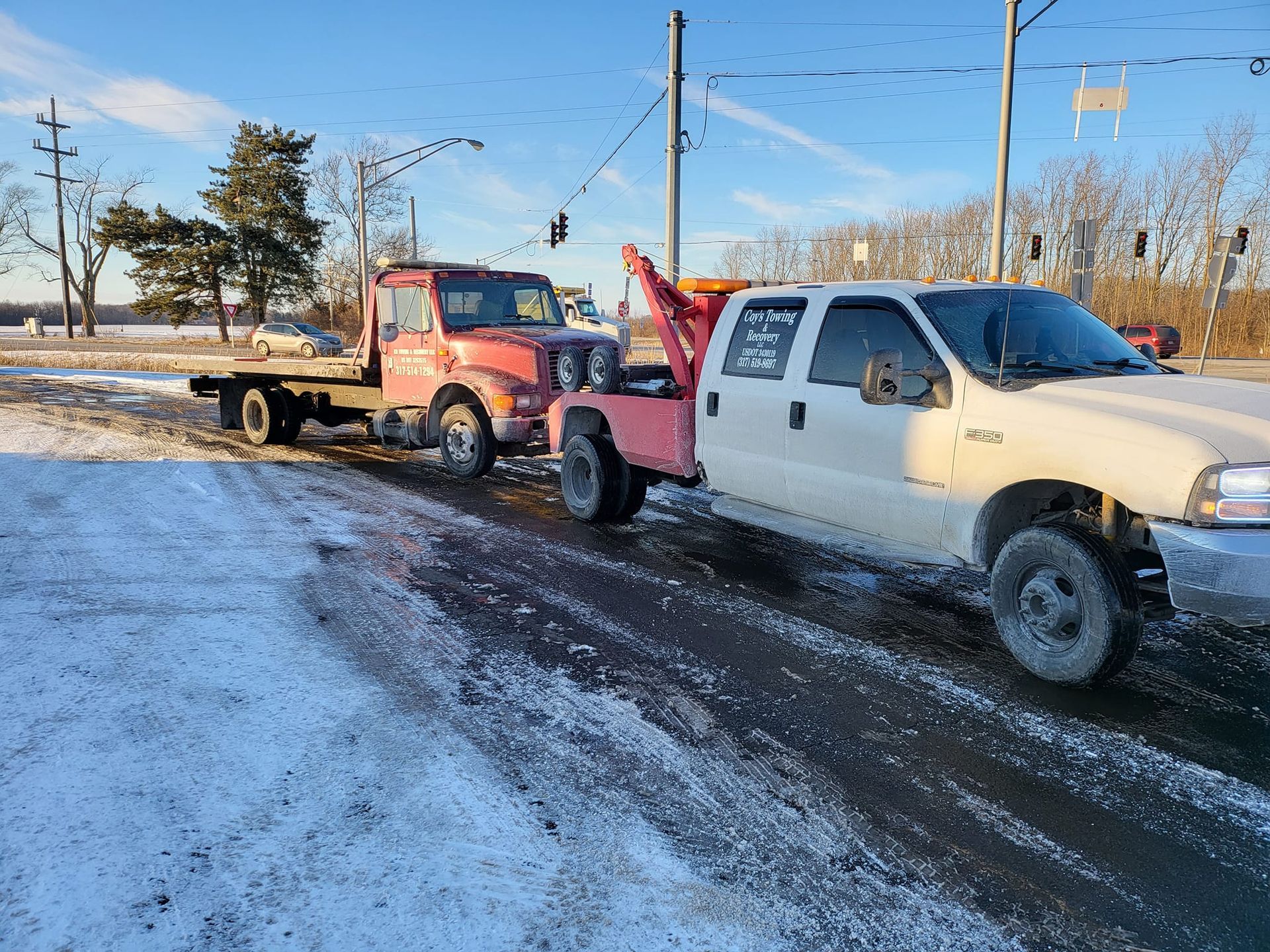 A white tow truck is towing a red truck on a snowy road.