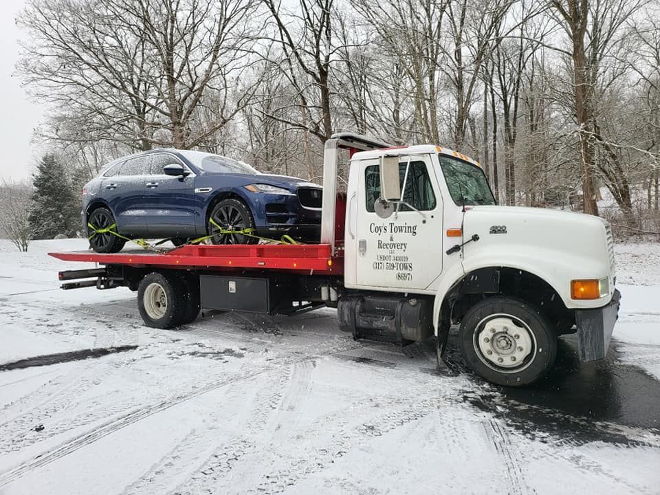 A tow truck is towing a blue car in the snow.