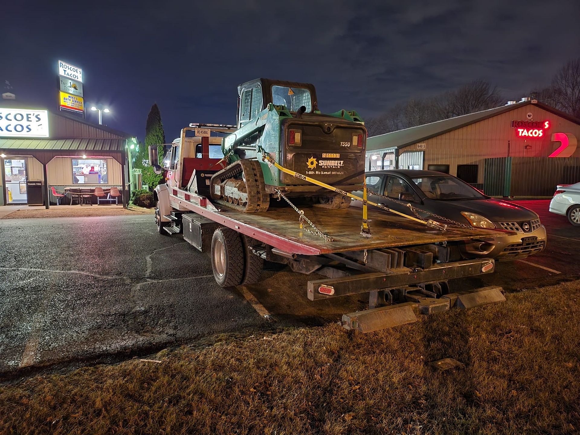 A tow truck is carrying a tractor on the back of it.