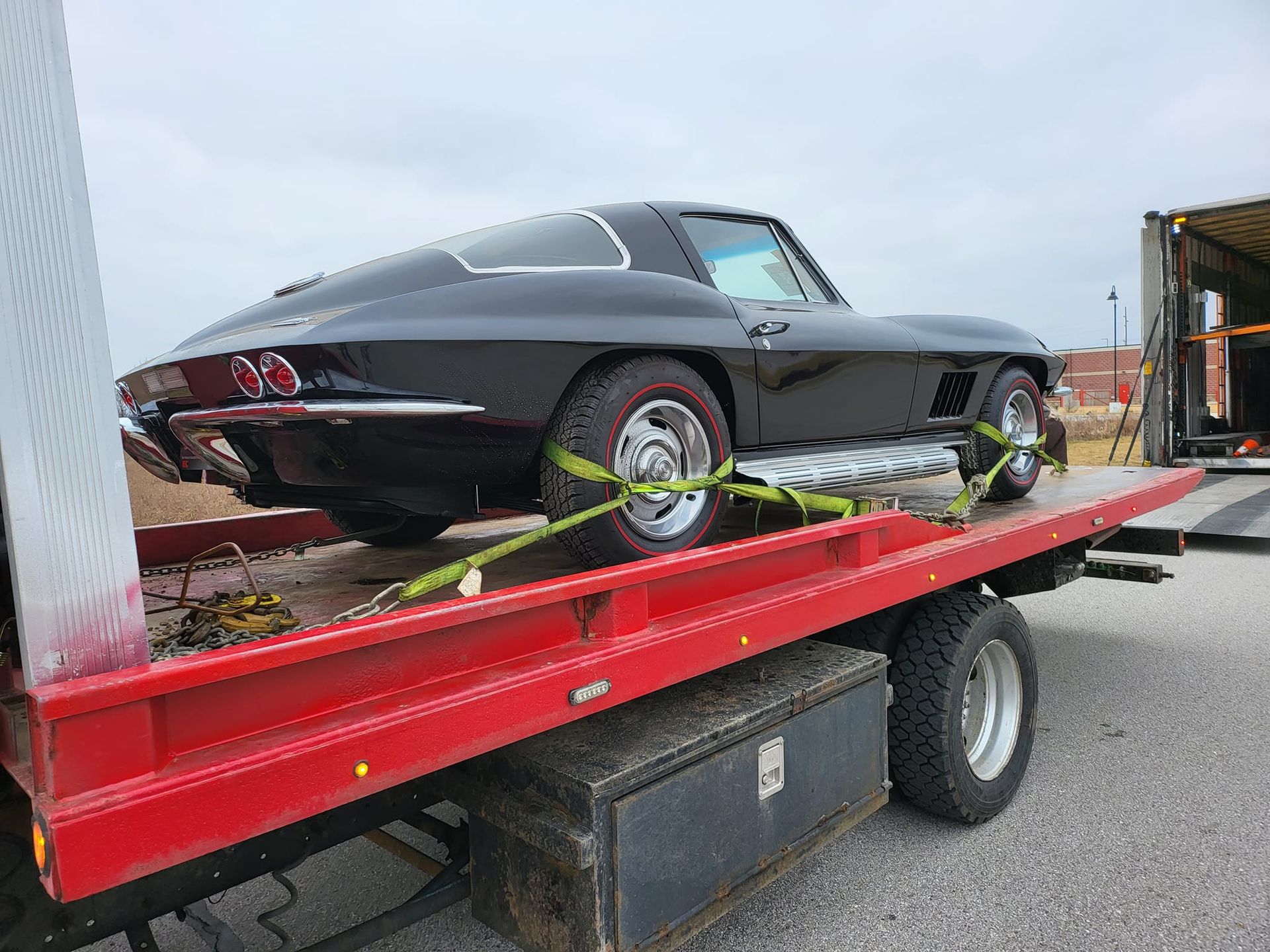 A black corvette is sitting on top of a red tow truck.