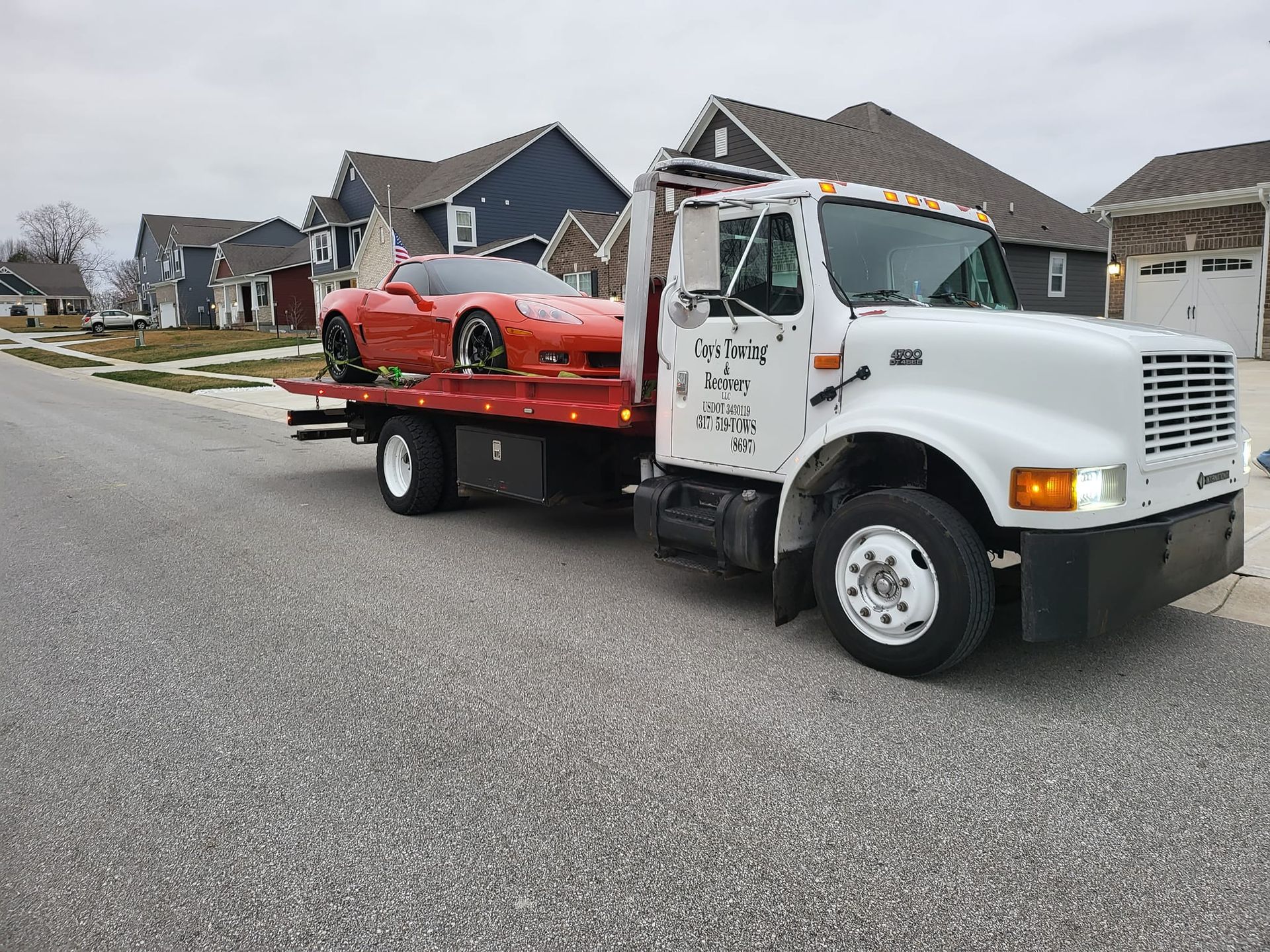 A tow truck is towing a red sports car down a street.