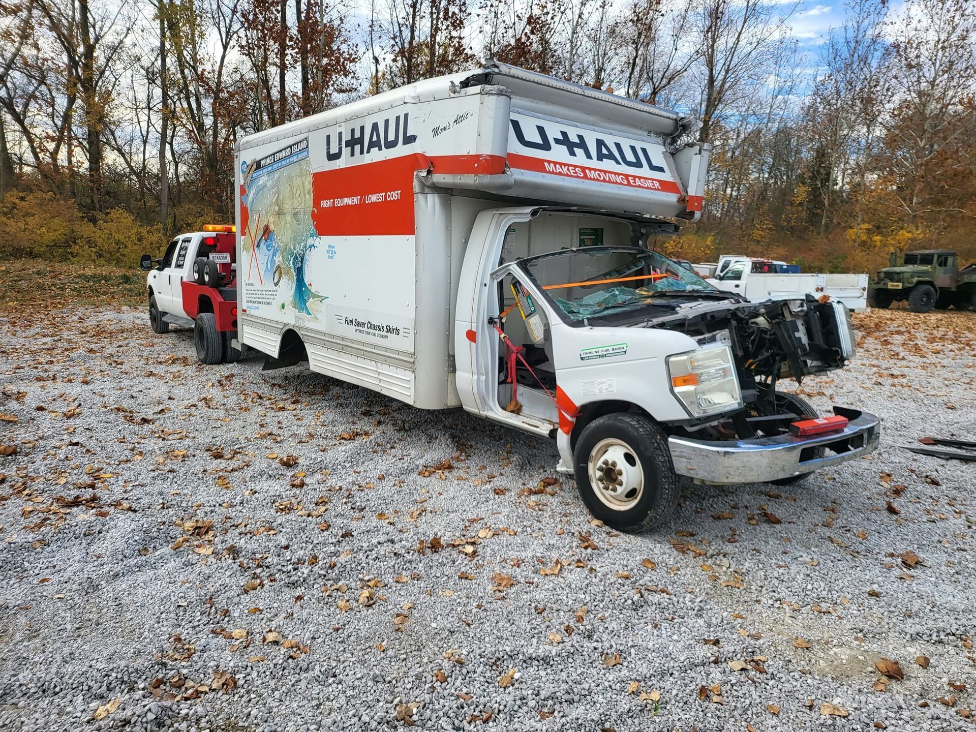 A uhaul truck is sitting in a gravel lot next to a tow truck.