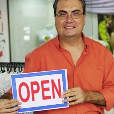 A man in an orange shirt is holding an open sign