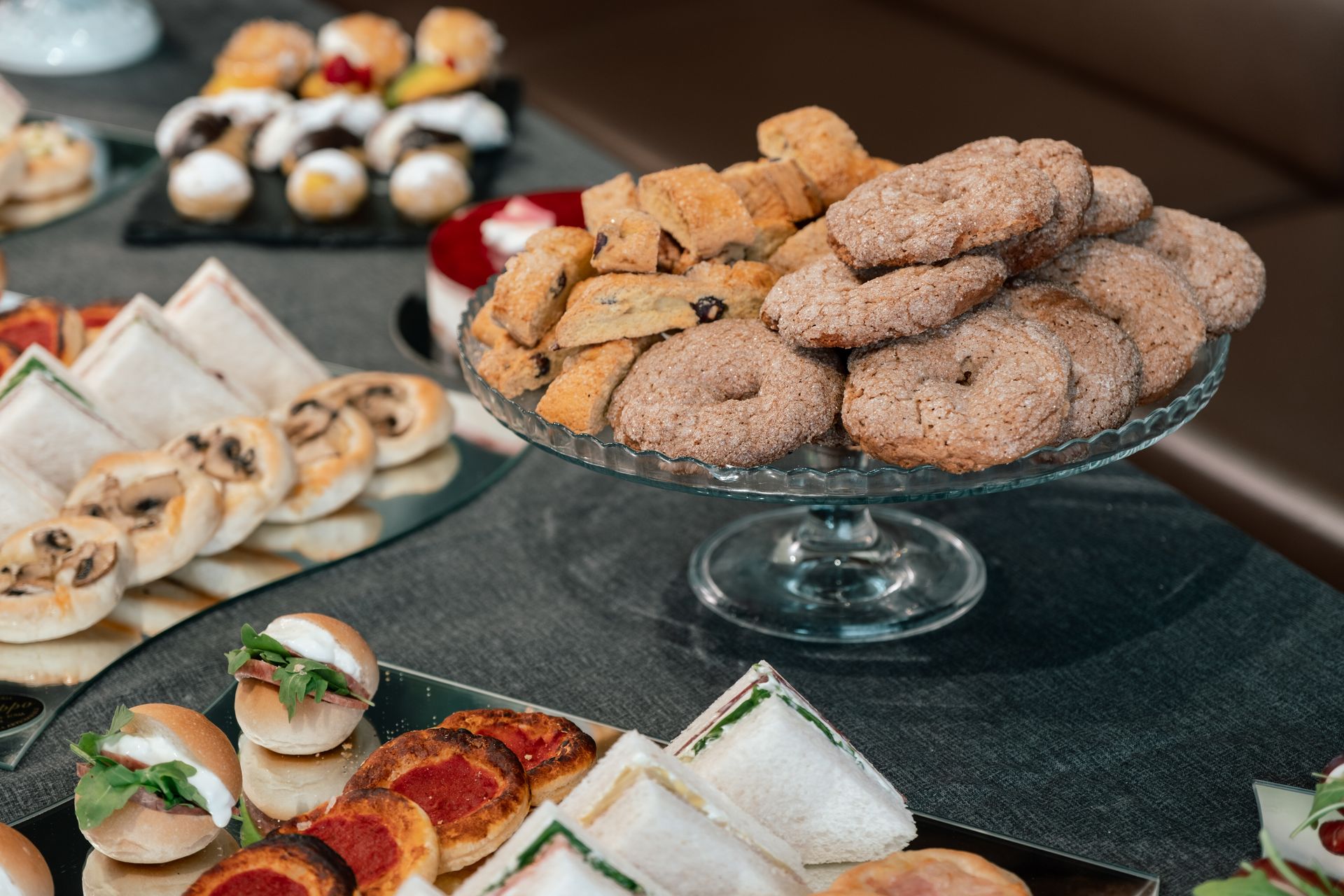 Assortimento di pasticcini e tramezzini disposti su vassoi a un tavolo da buffet.