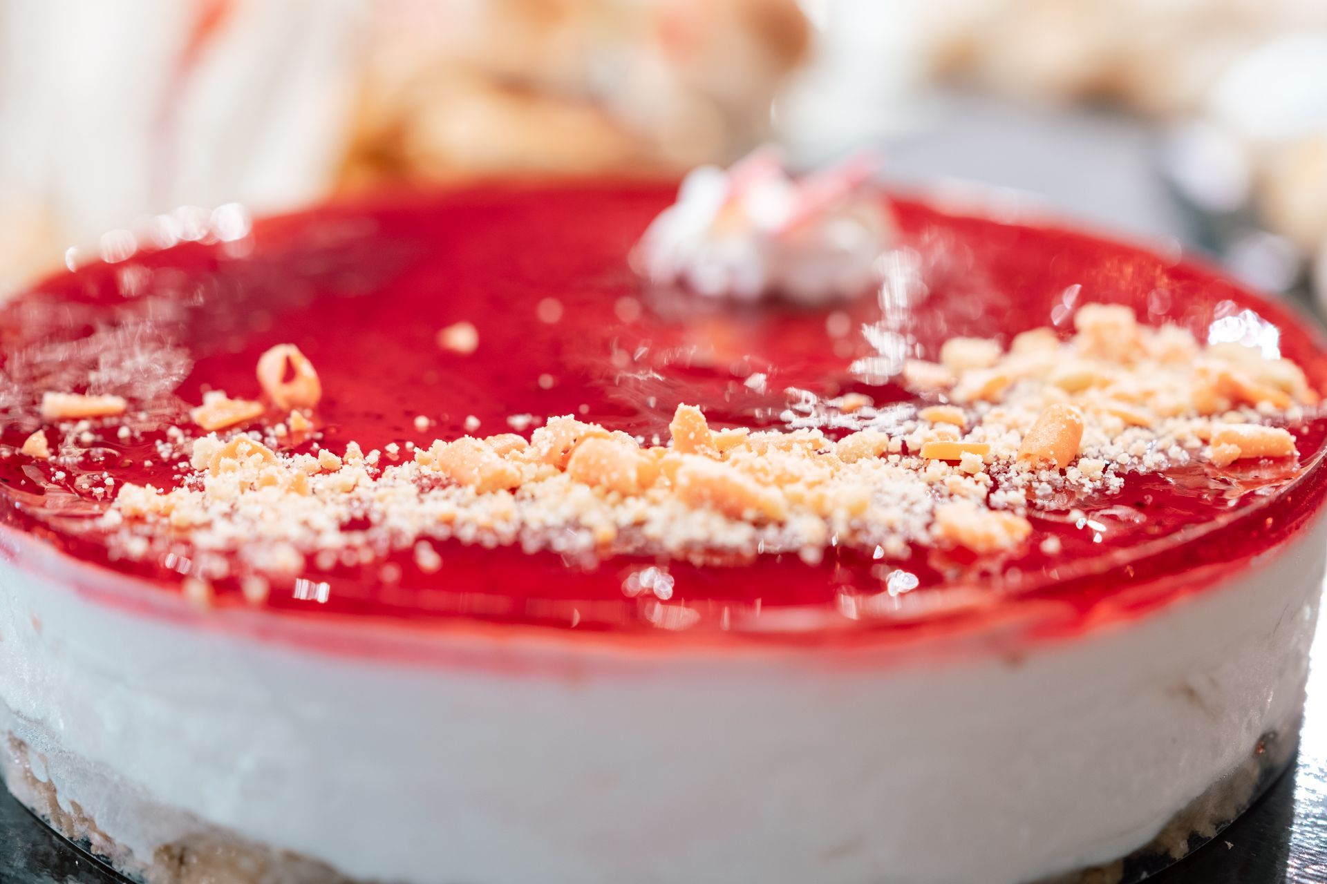 Cheesecake glassata di rosso con strato di crema bianca e copertura di briciole, servita su un piatto da dessert.