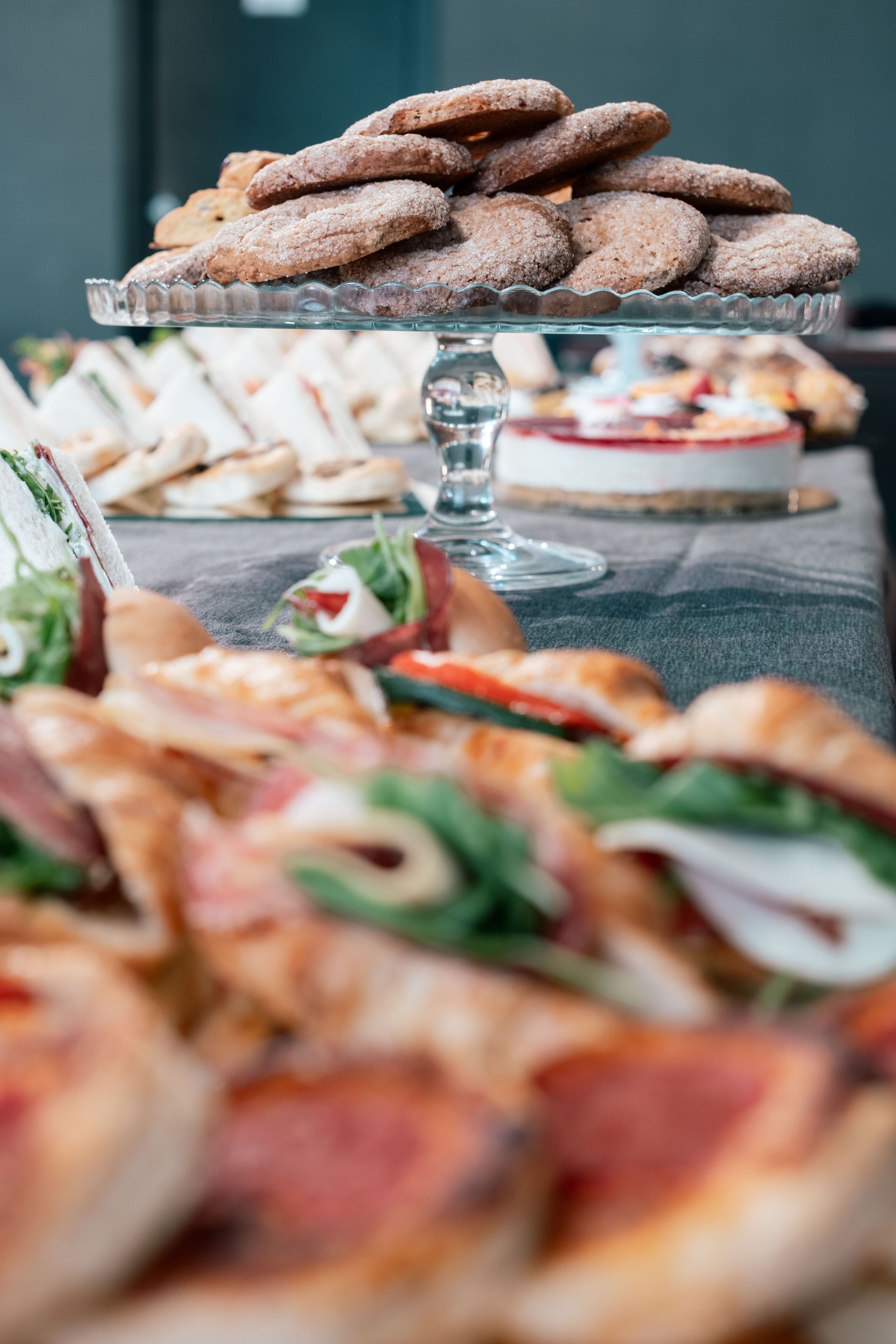Su un tavolo si possono ammirare diversi dessert, tra cui una pila di pasticcini e una pizza sfocata in primo piano.