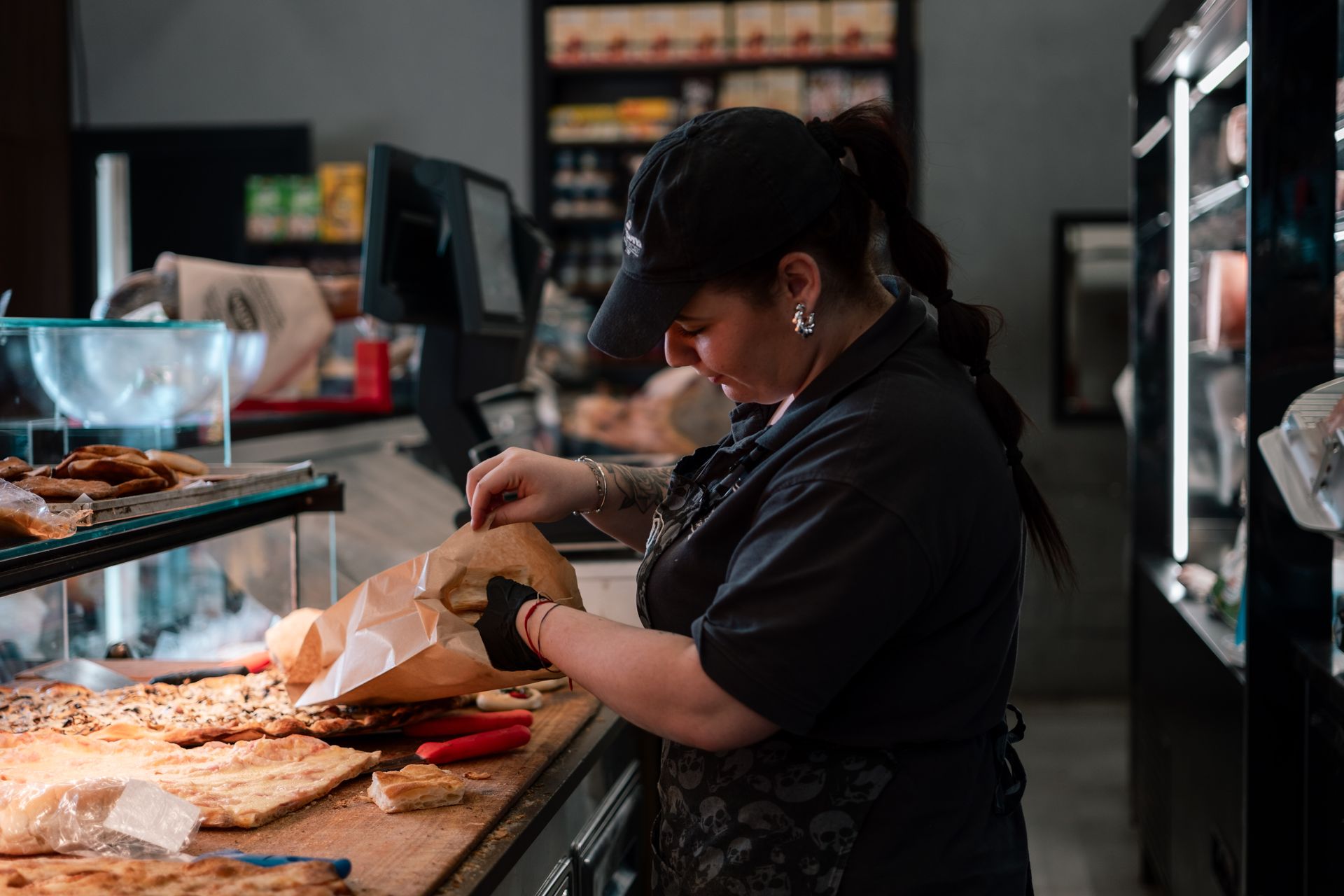 Un'addetta al banco di una panetteria confeziona un dolce in un sacchetto di carta dietro una vetrina.