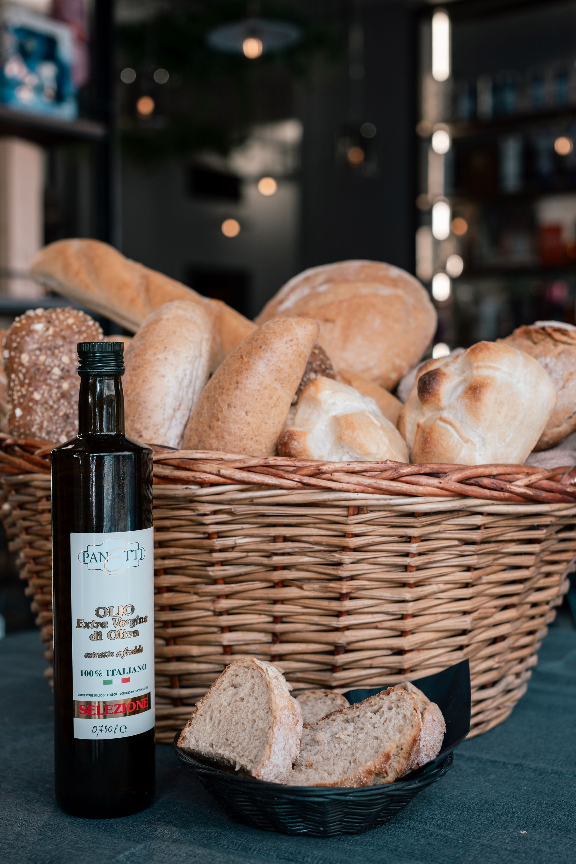 Una bottiglia di olio d'oliva accanto a un cesto di vimini con pagnotte e pane a fette su un tavolo.