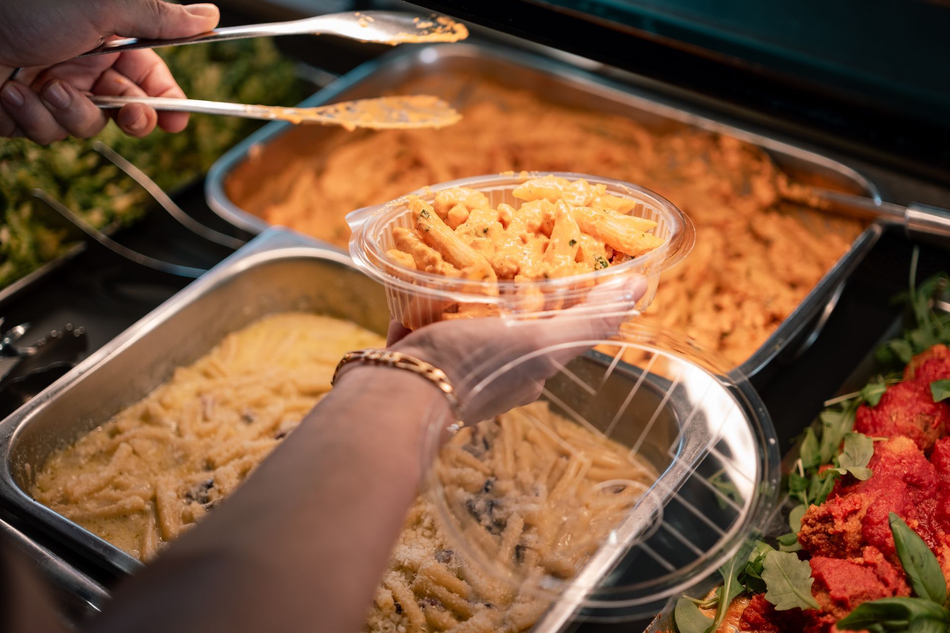 Mani che servono maccheroni e formaggio da un buffet in un bicchiere di plastica trasparente.