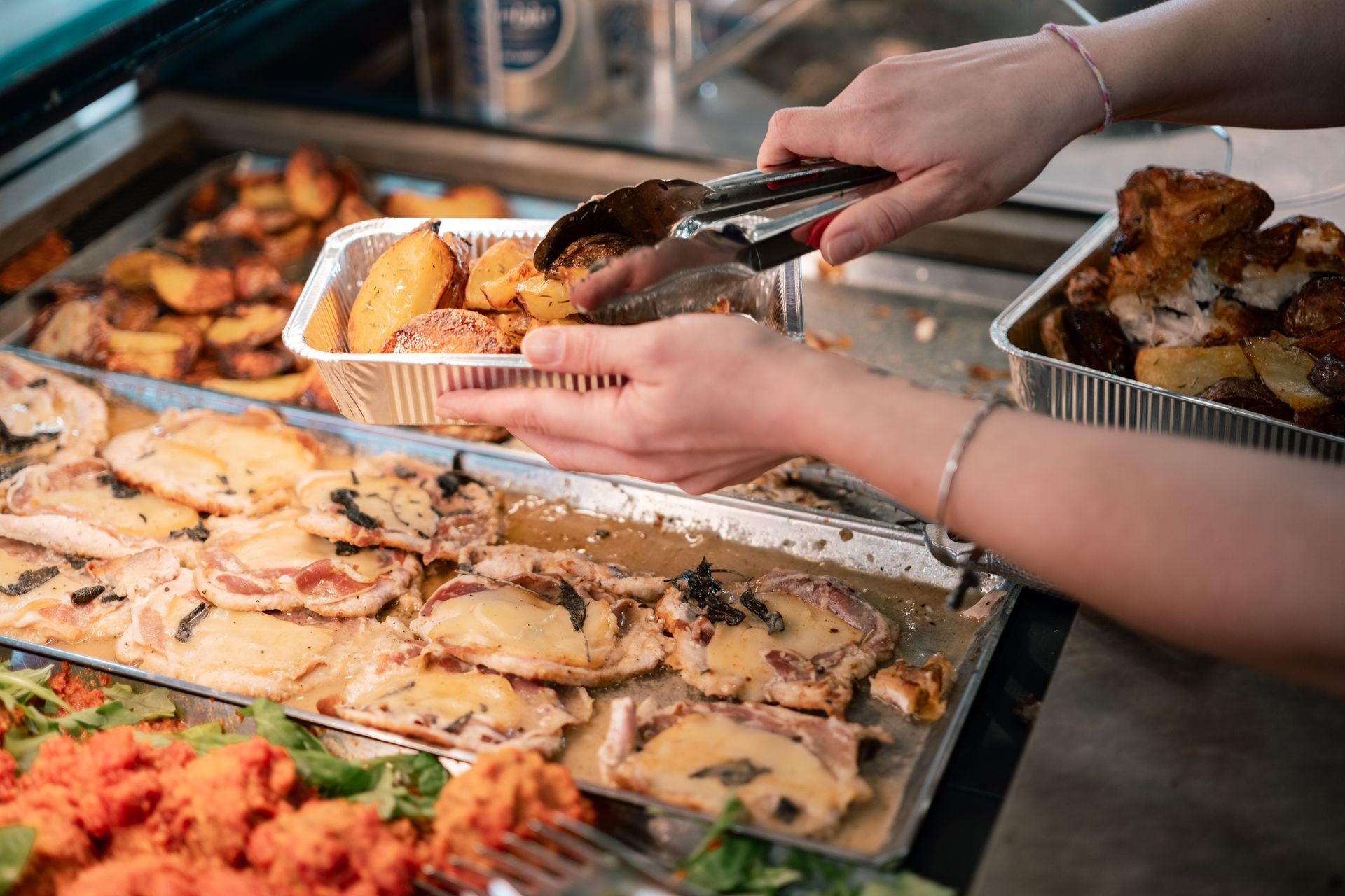 Mani che servono cibo da un vassoio da buffet con patate arrosto e piatti di pasta