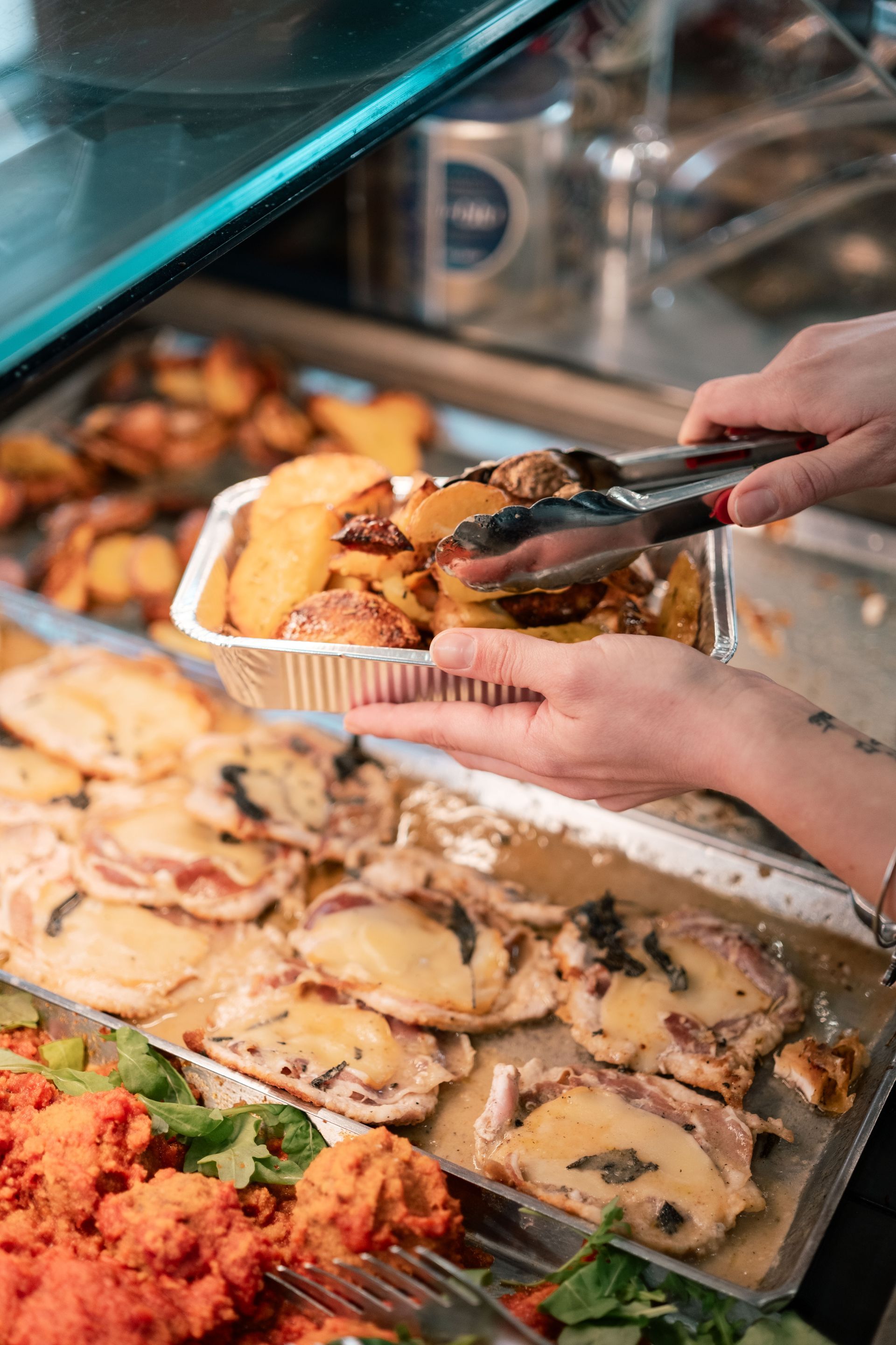 Mani che servono il cibo da un vassoio del buffet con delle pinze al bancone di una mensa.