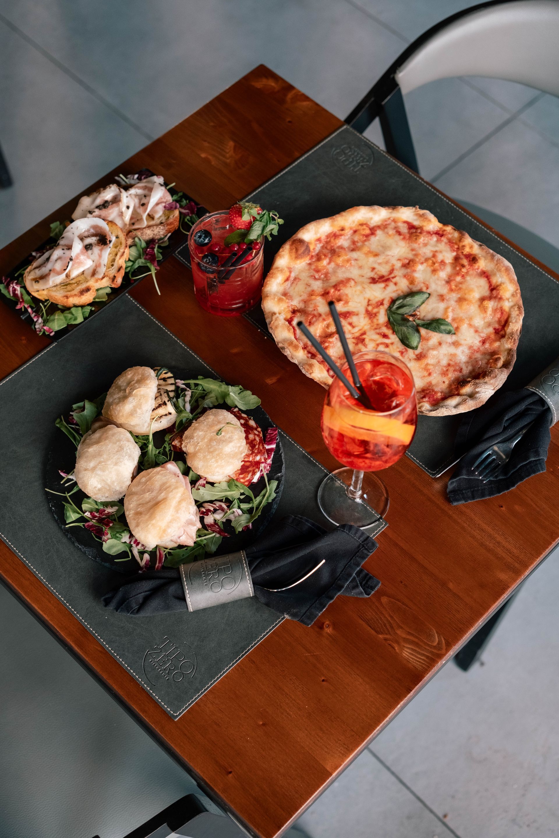 Vista dall'alto di un tavolo di legno con diverse pietanze, tra cui pizza, insalata e piccoli antipasti.
