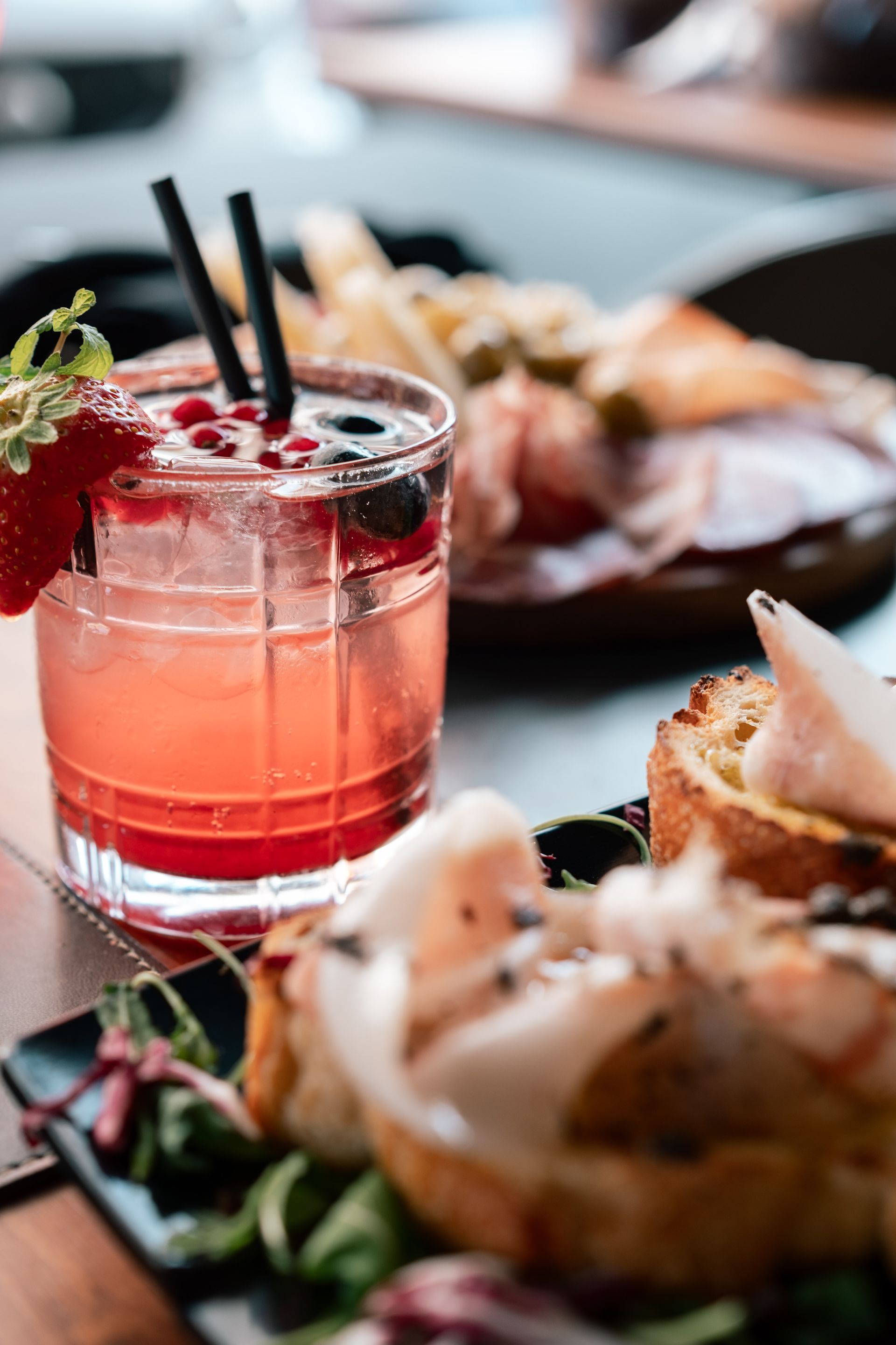 Cocktail rosa con frutti di bosco e cannucce accanto a piccoli antipasti su un tavolo
