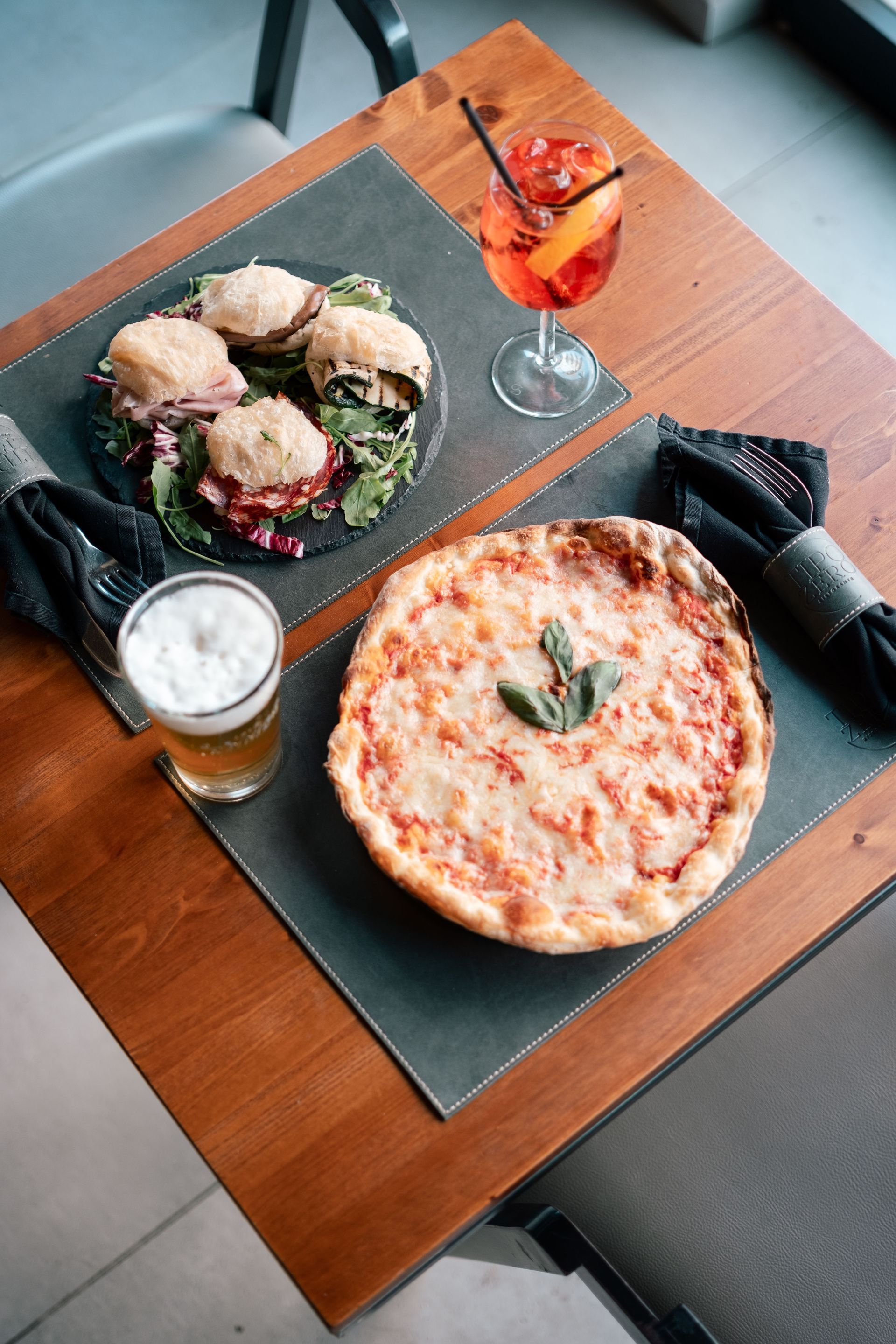 Pizza, insalata e bevande su un tavolo di legno con tovagliette nere.