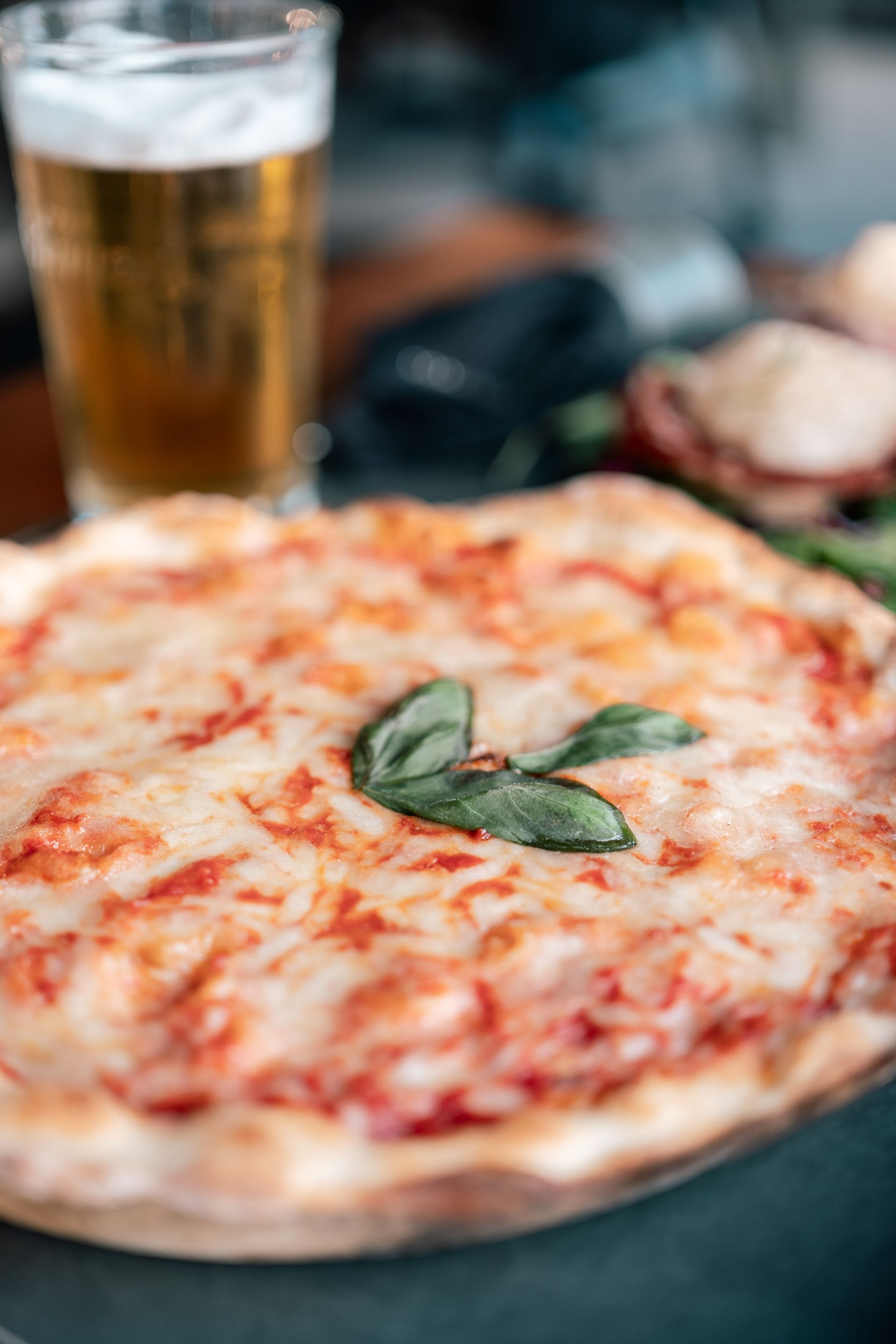 Una pizza Margherita al basilico su un tavolo, con un bicchiere di birra sullo sfondo.