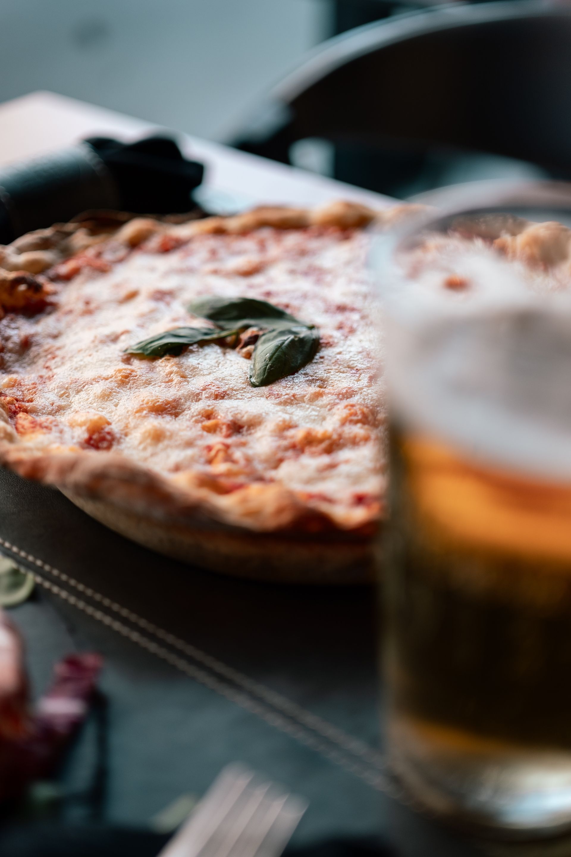 Pizza su un tavolo scuro accanto a un bicchiere di birra appannato