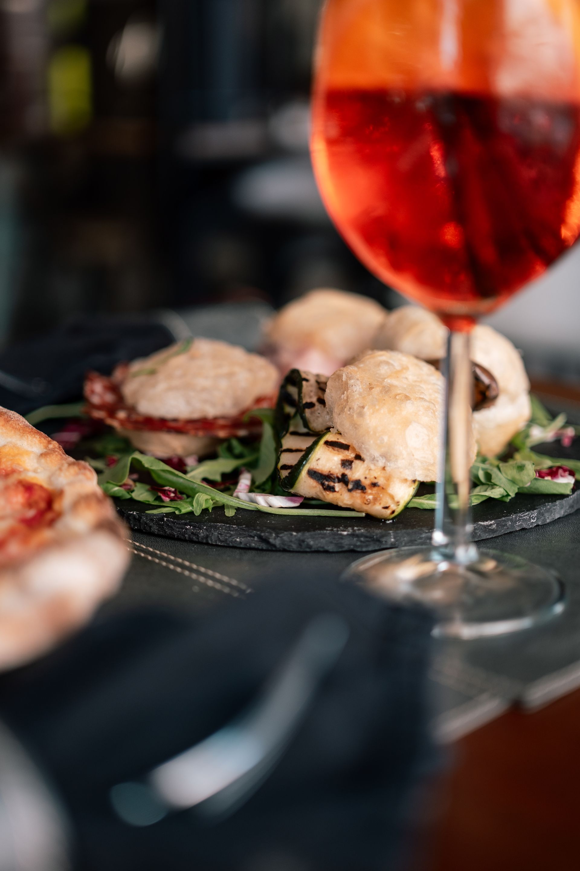 Antipasti serviti con verdure su un tavolo accanto a un bicchiere di bevanda rossa.