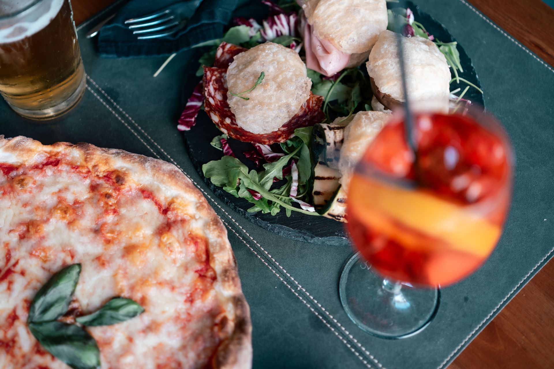 Pizza e cocktail su un tavolo scuro con insalata e bevande nelle vicinanze.