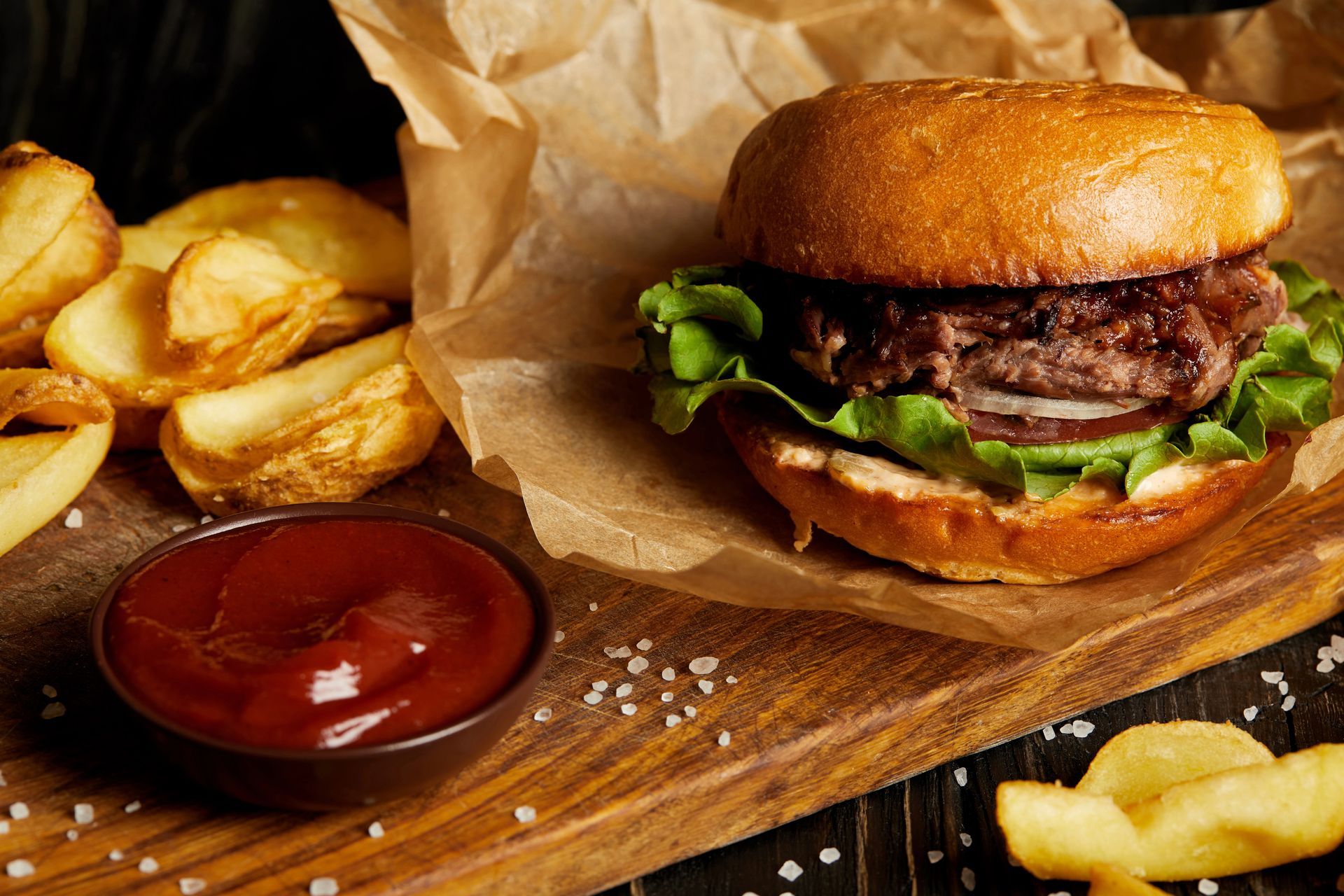 Hamburger con patatine fritte e ketchup su un tagliere di legno, avvolto nella carta.
