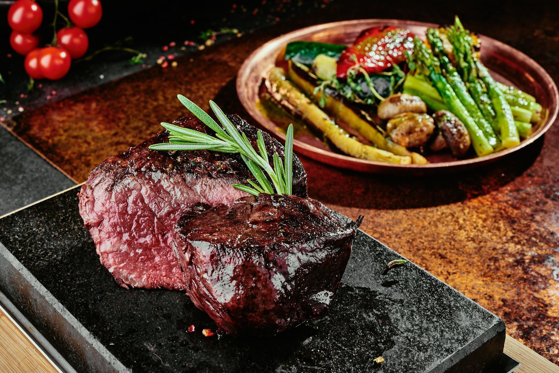Bistecca alla griglia con rosmarino e verdure arrostite su un piatto di ardesia scura.