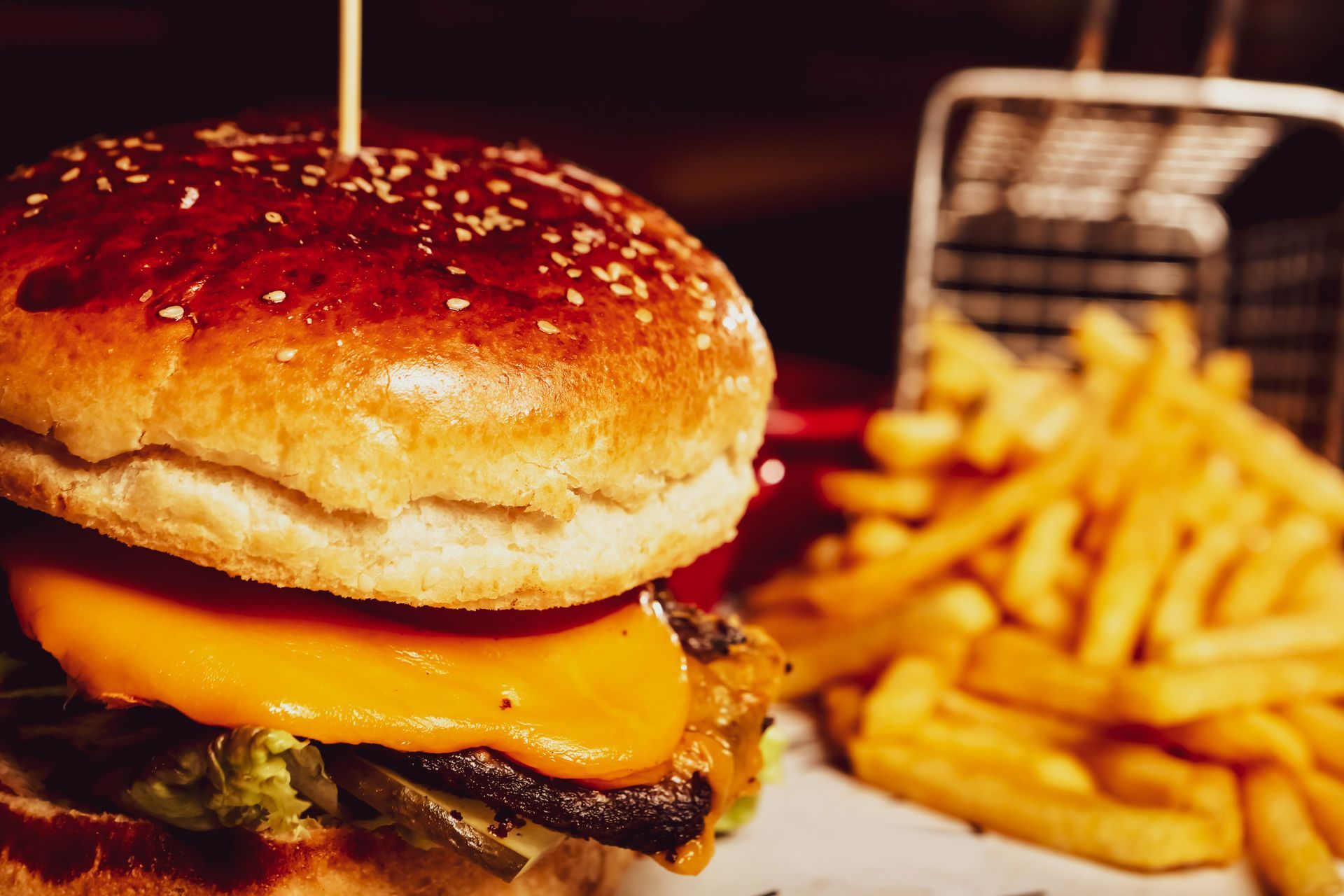 Primo piano di un cheeseburger con patatine fritte su un vassoio, illuminato da una luce calda.