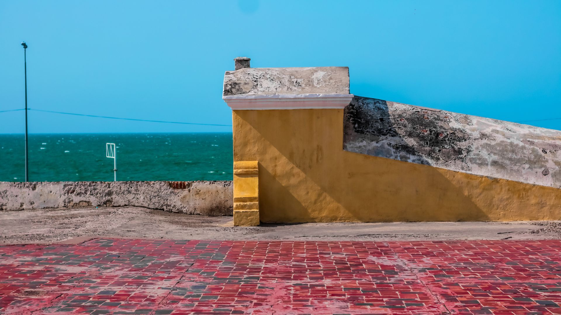 Seaside concrete ramp and wall beside a red paved promenade under a bright blue sky