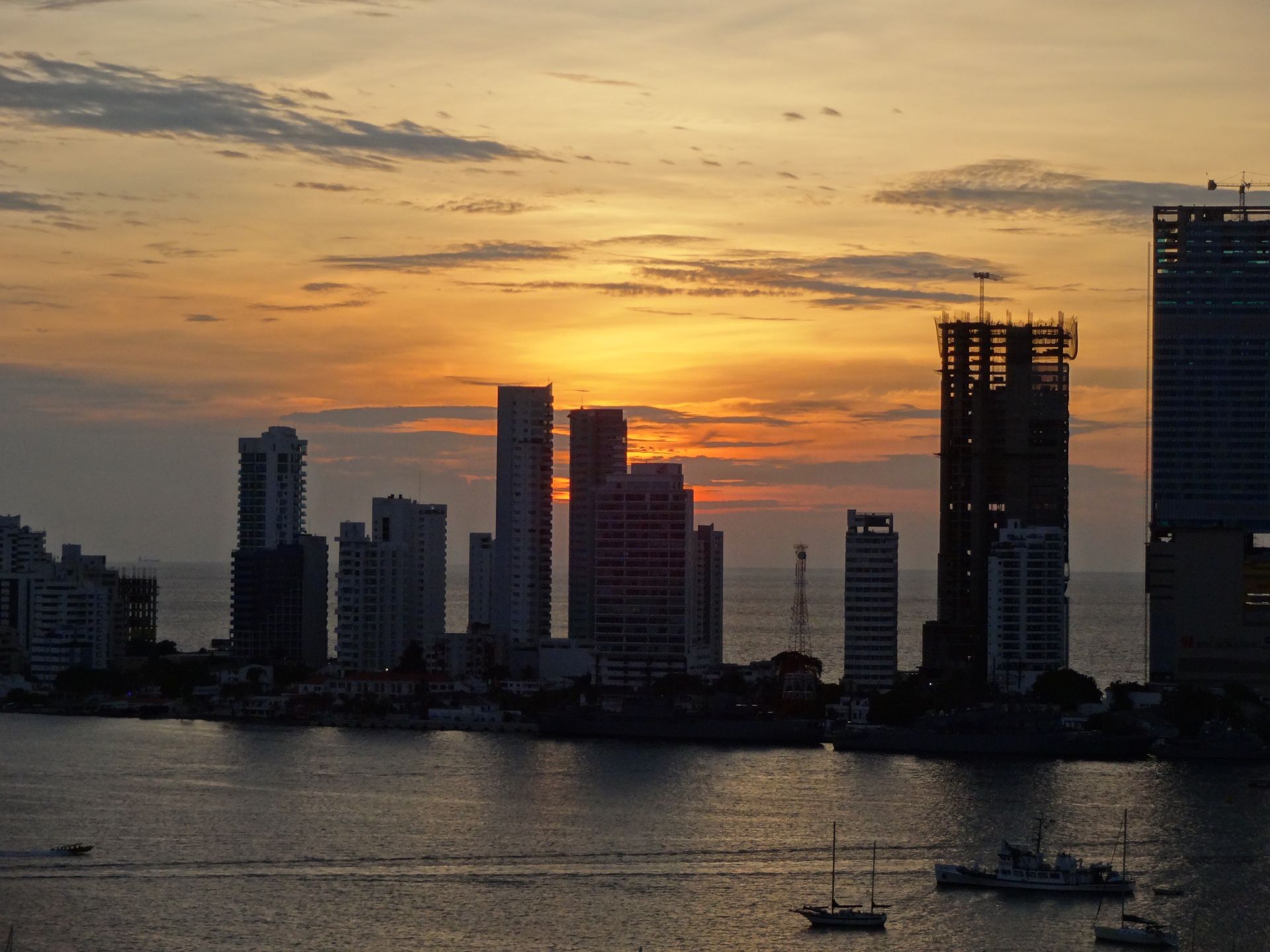 City skyline at sunset over calm water, with silhouetted high-rises and glowing orange clouds