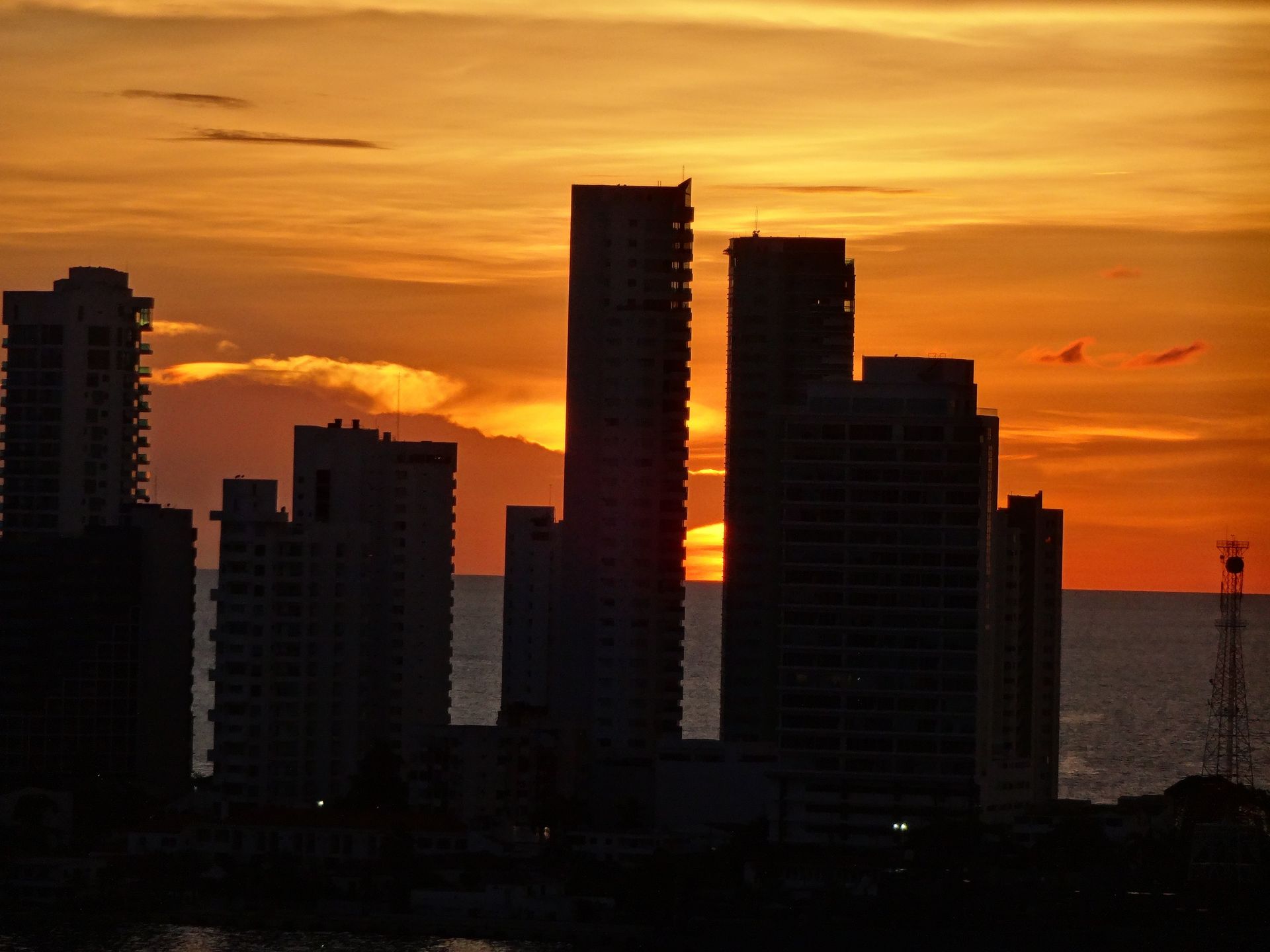 Silhouetted city skyline at sunset with orange sky over the water