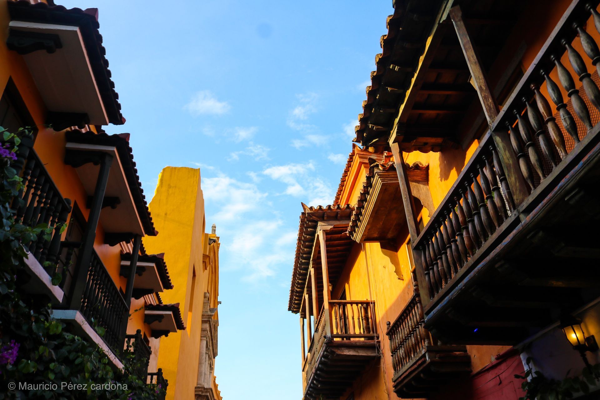 Colorful narrow street with wooden balconies and warm sunlight under a blue sky