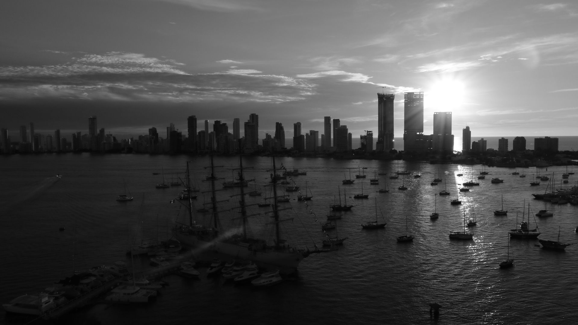 Sunset over a city skyline with boats on calm water in the foreground